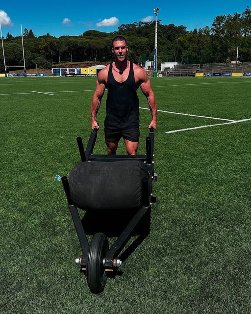 Jay Gardner is pushing a wheelbarrow on a field