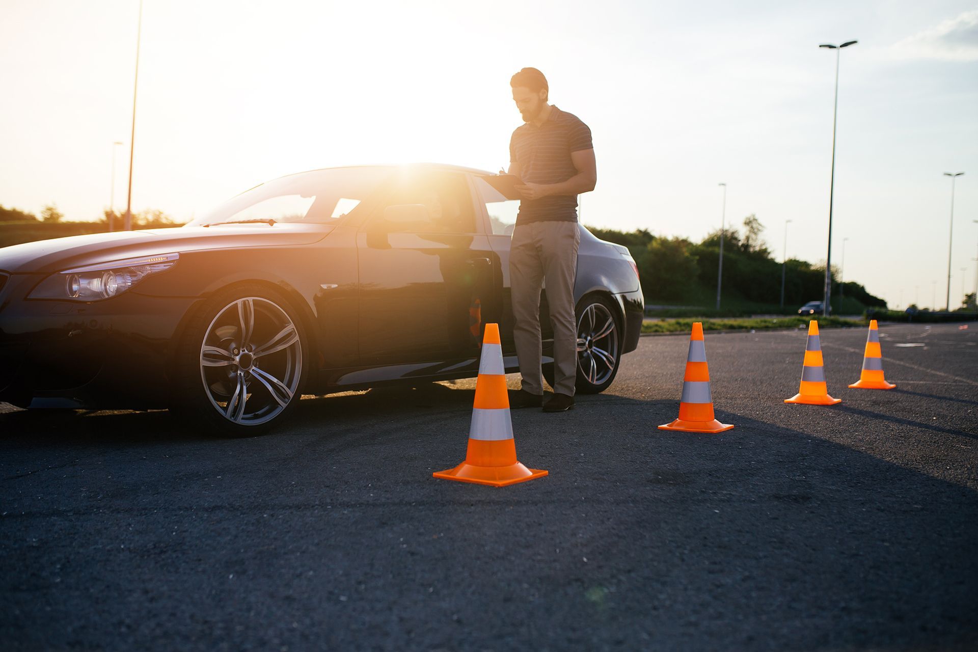 A man is standing next to a car surrounded by traffic cones.