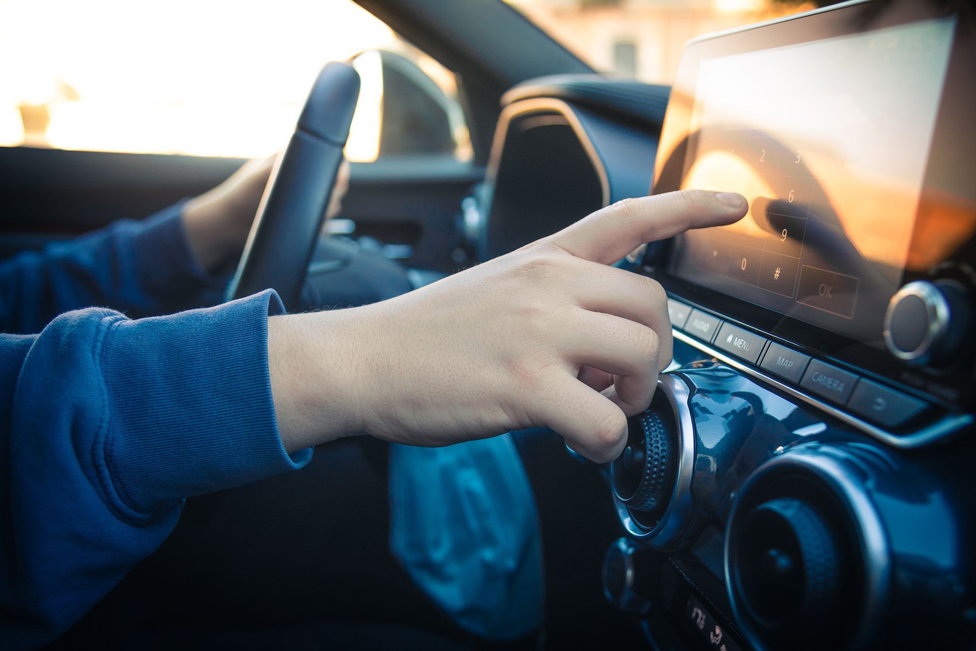 A person is driving a car and pointing at the radio.