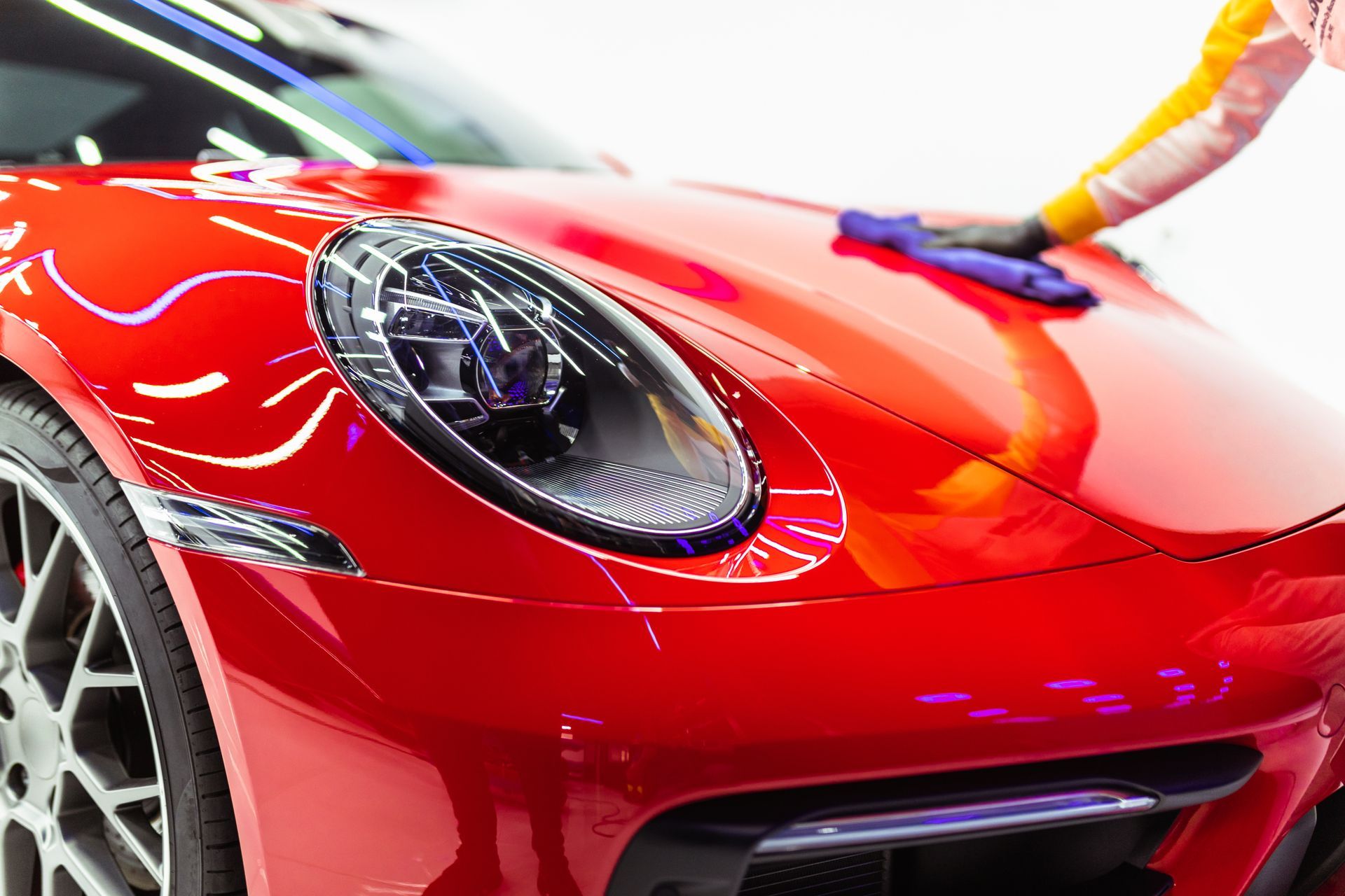 A person is polishing the hood of a red sports car.