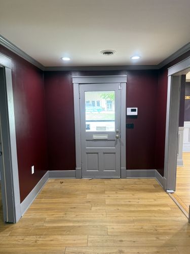 Empty hallway with burgundy walls, wood floor, and a gray front door.