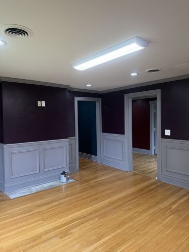Empty room with hardwood floor, dark walls, white wainscoting, and an open doorway under a ceiling light.