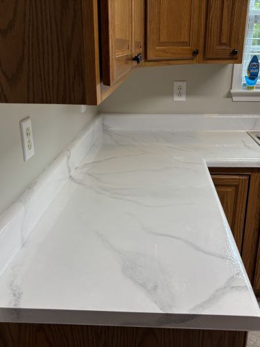 White marble-look kitchen countertop with light gray veining and wood cabinets above and below