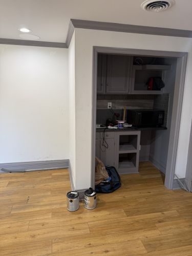 Empty room with hardwood floor and a small recessed desk nook, with a paint can and bag near the doorway.