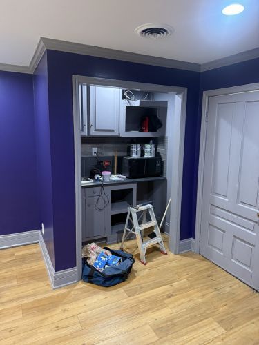 Small kitchen nook under renovation with cabinets, countertop, step stool, and tools against a purple wall