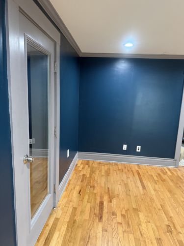 Empty room with blue accent wall, hardwood floor, and a glass-paneled door on the left.
