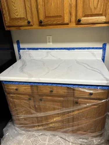 White countertop wrapped in plastic, taped off with blue painter’s tape, over wooden kitchen cabinets.