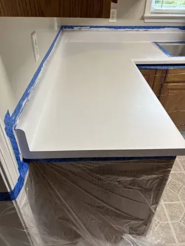 Kitchen countertop being refinished with blue painter’s tape and plastic sheeting covering the cabinets below