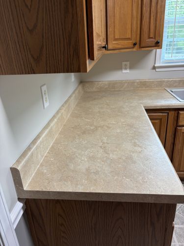 Kitchen countertop with beige stone surface and wooden cabinets beside a window.