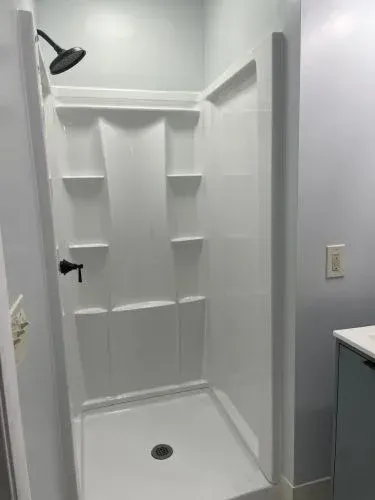 White walk-in shower with built-in shelves, showerhead, and a small drain in a light gray bathroom.