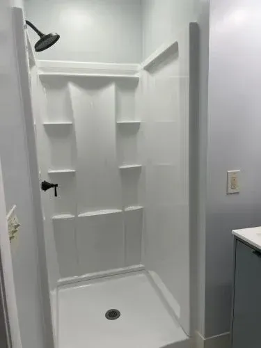 White walk-in shower with built-in shelves, black showerhead, and light gray walls.