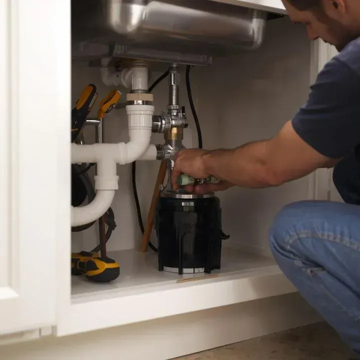 Person installing a garbage disposal under a kitchen sink.