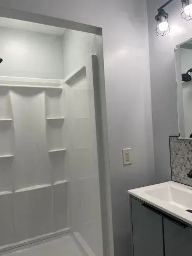 Bathroom with shower alcove, gray walls, and white vanity with sink and mirror.