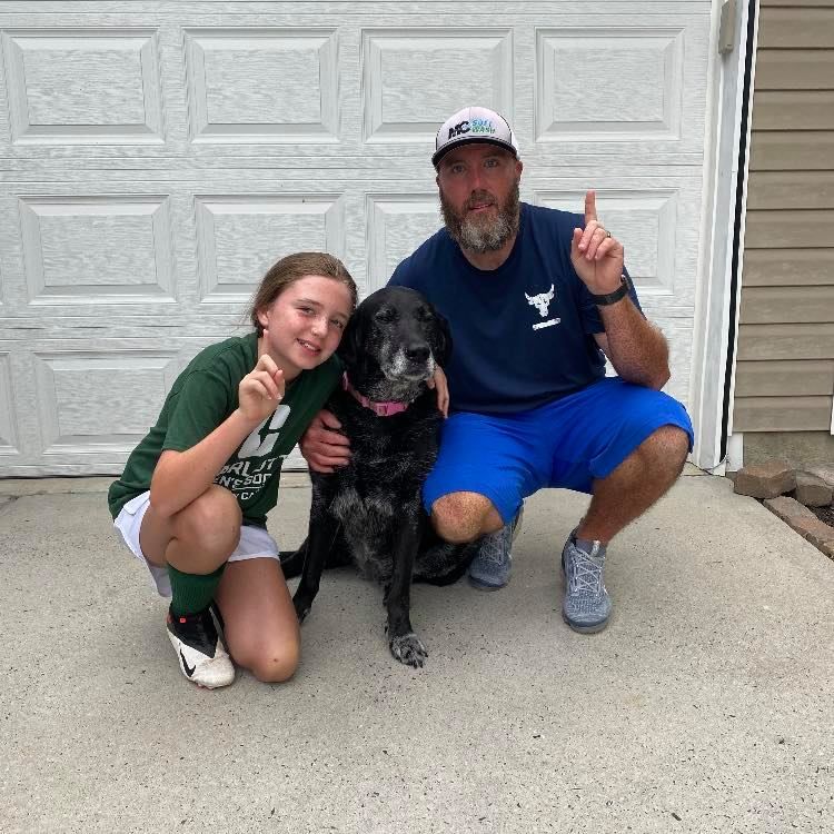 A man and a girl are posing for a picture with their dog