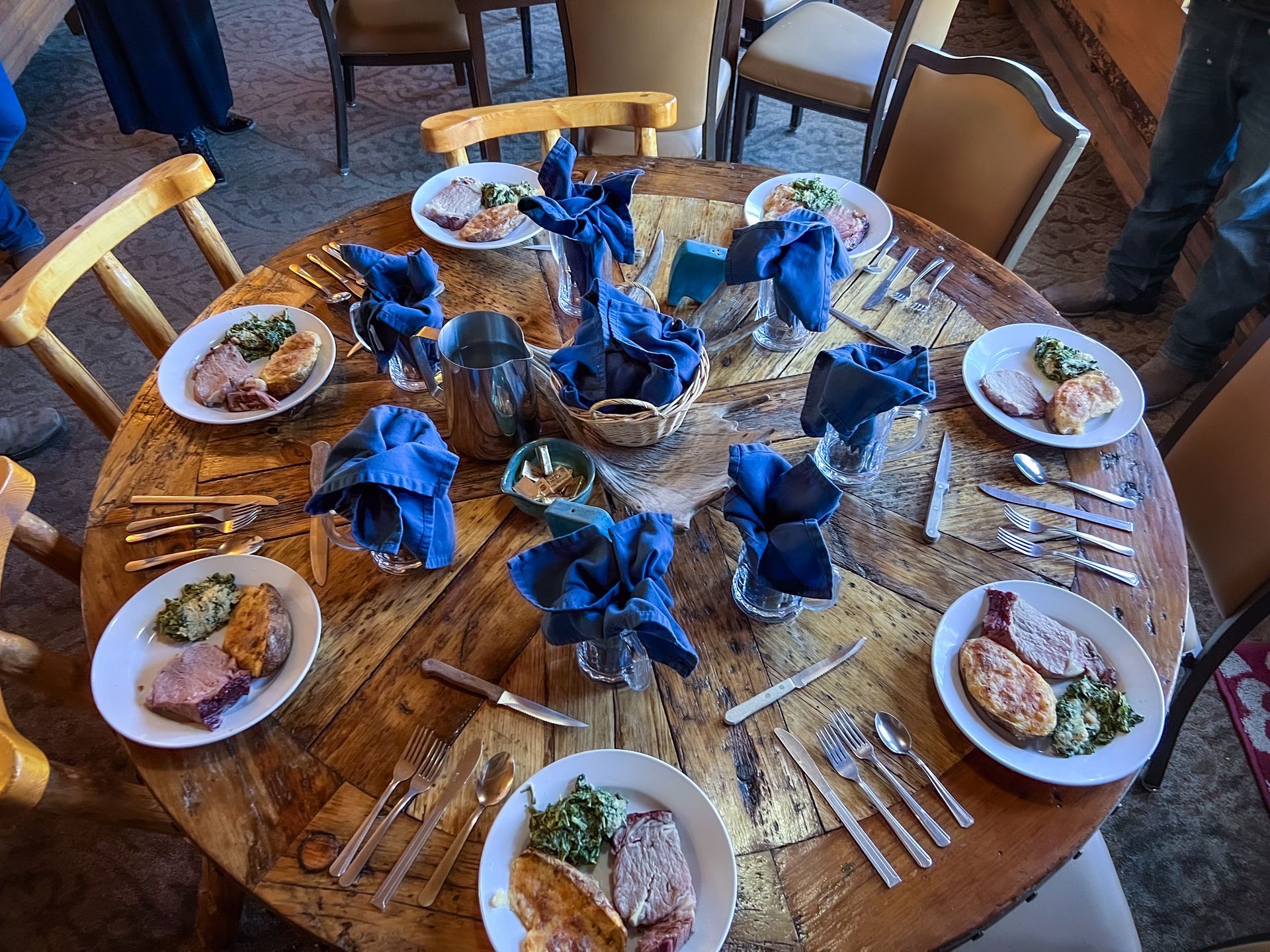 Round dining table set with plates, silverware, and blue napkins