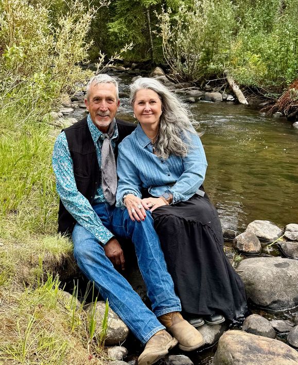 Couple sitting on rocks by a wooded stream, smiling in blue clothing.
