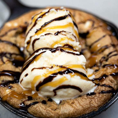 Warm cookie skillet topped with vanilla ice cream and drizzled chocolate sauce