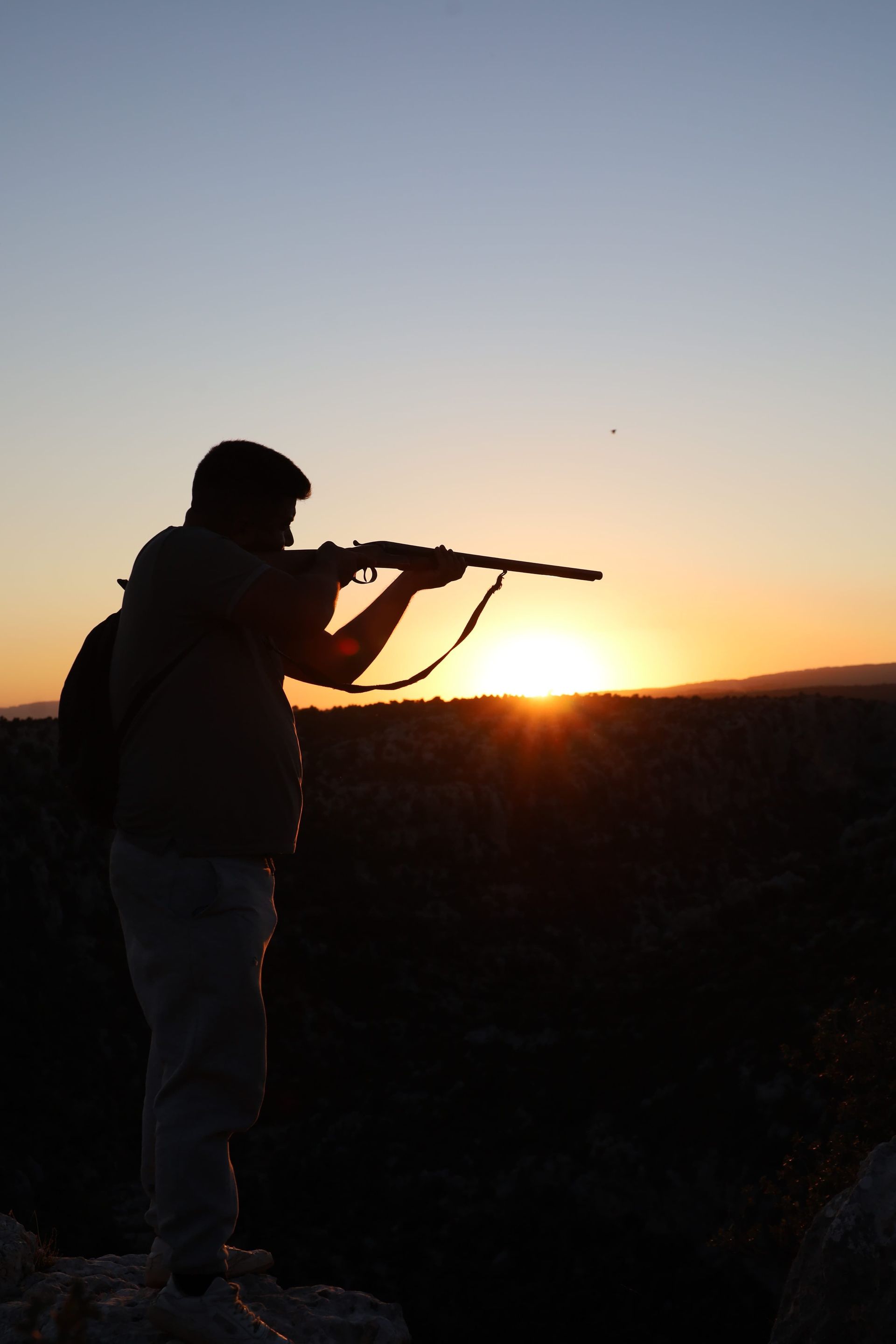 Silhouetted person aiming a rifle at sunset in an open field