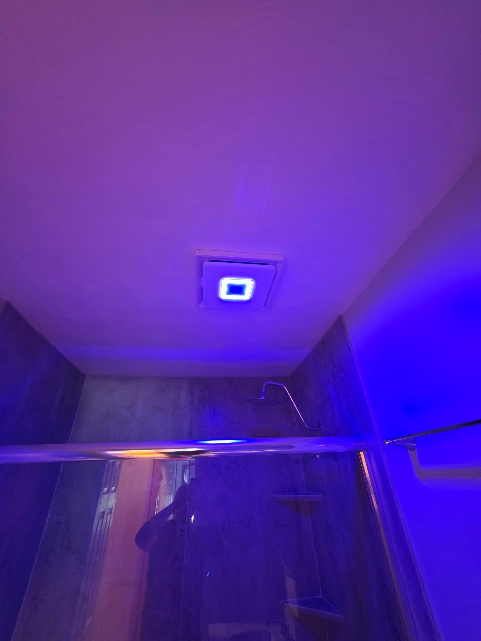 Blue-lit shower stall, with overhead square light fixture. Glass door on the right.