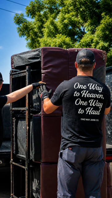 Volunteers loading a stacked couch onto a moving truck outdoors under a sunny sky