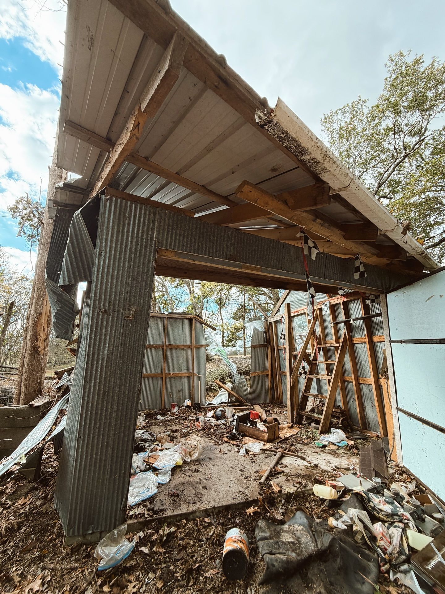 Collapsed rustic shed with a corrugated metal roof, leaning posts, and debris scattered underneath.