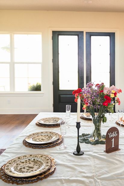Festive dining table with floral centerpiece, patterned plates, and black candlesticks in a bright room
