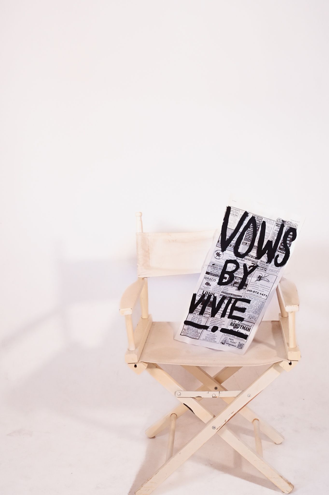 Wooden director’s chair with a black-and-white “Vogue” magazine cover leaning on it in a white studio.