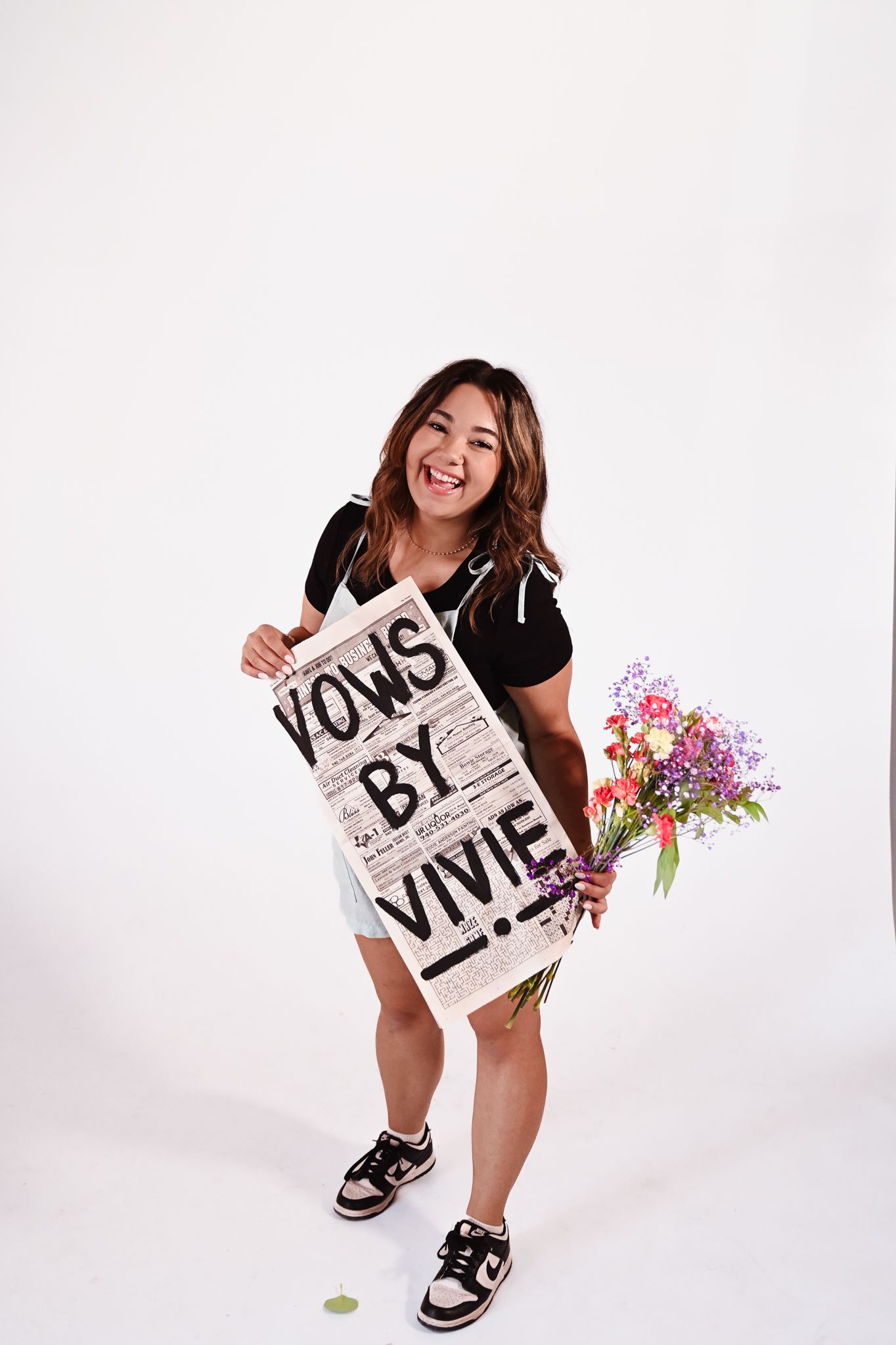 Woman holding a sign reading “DOGS BY VIV” beside a colorful bouquet on a white backdrop