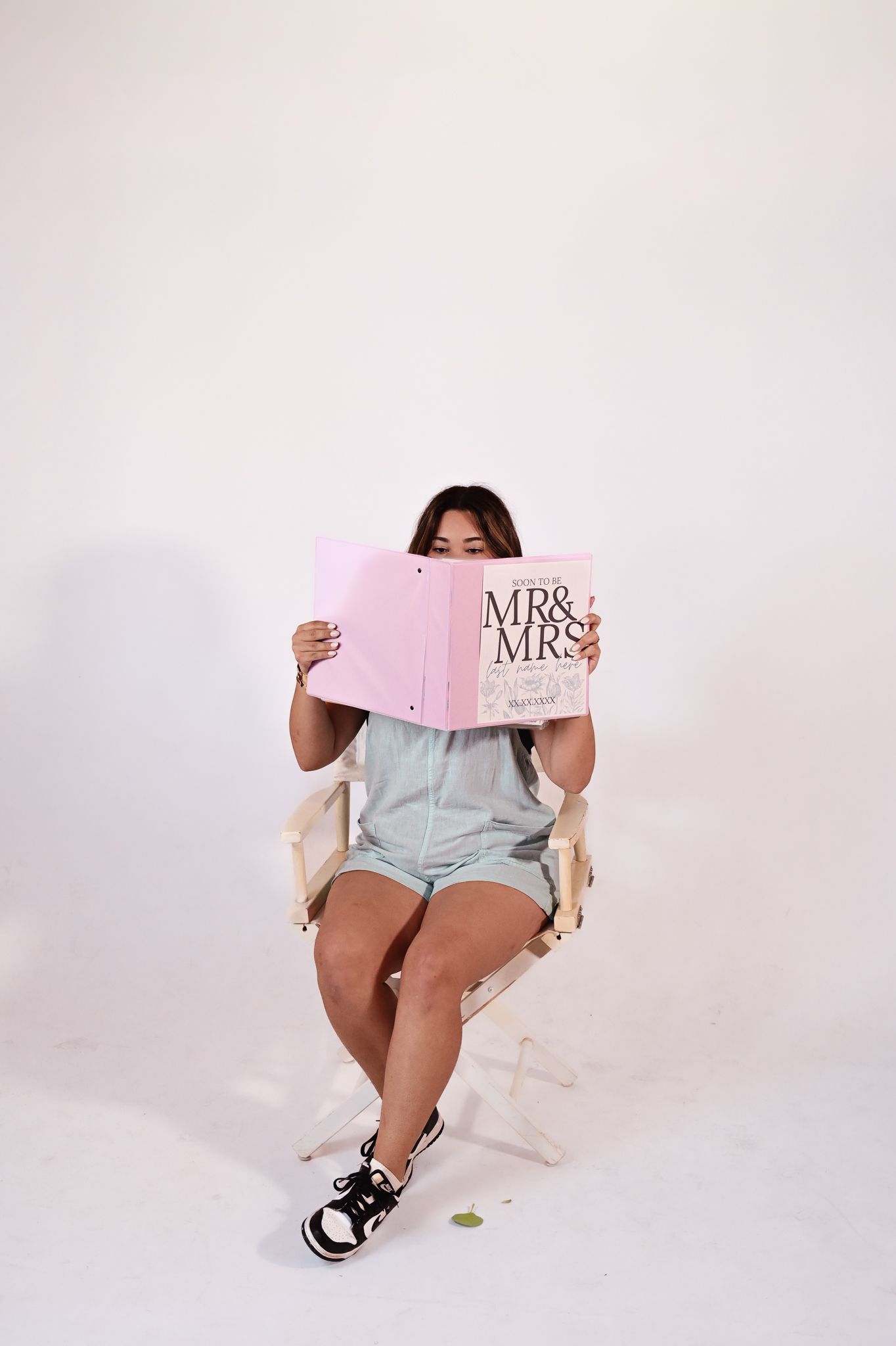 Person seated on a white chair, reading a pink book against a plain white background.