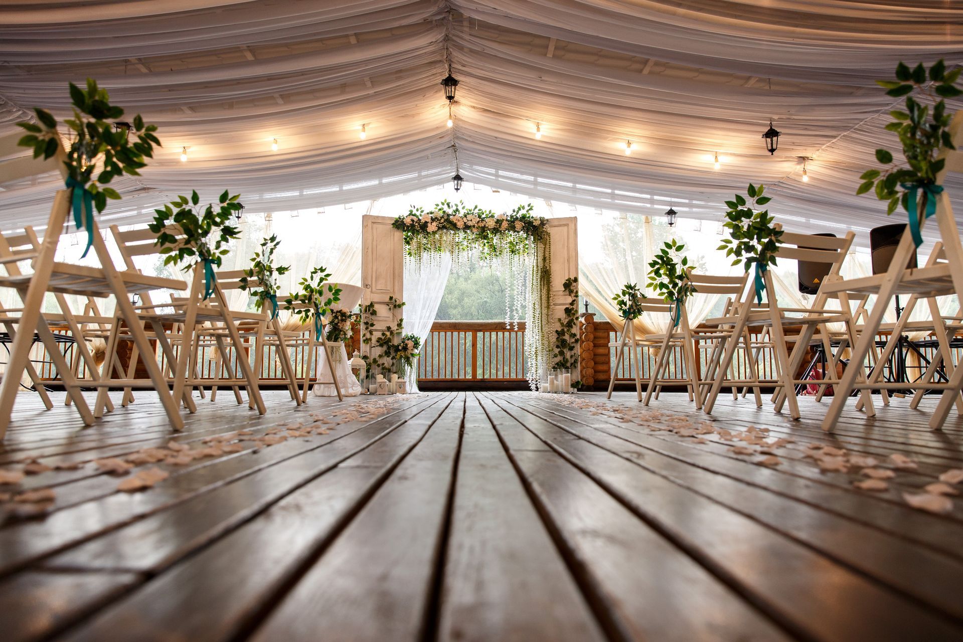 Rustic wedding tent with wooden floor, draped ceiling, and decorated tables and chairs at the aisle