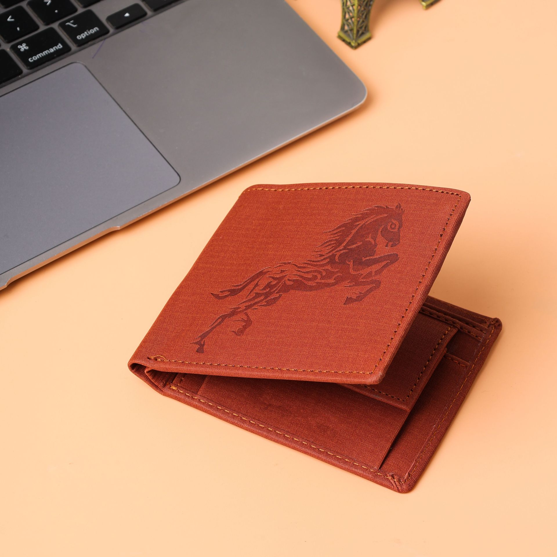 Two red textured wallets beside a silver laptop on a peach surface