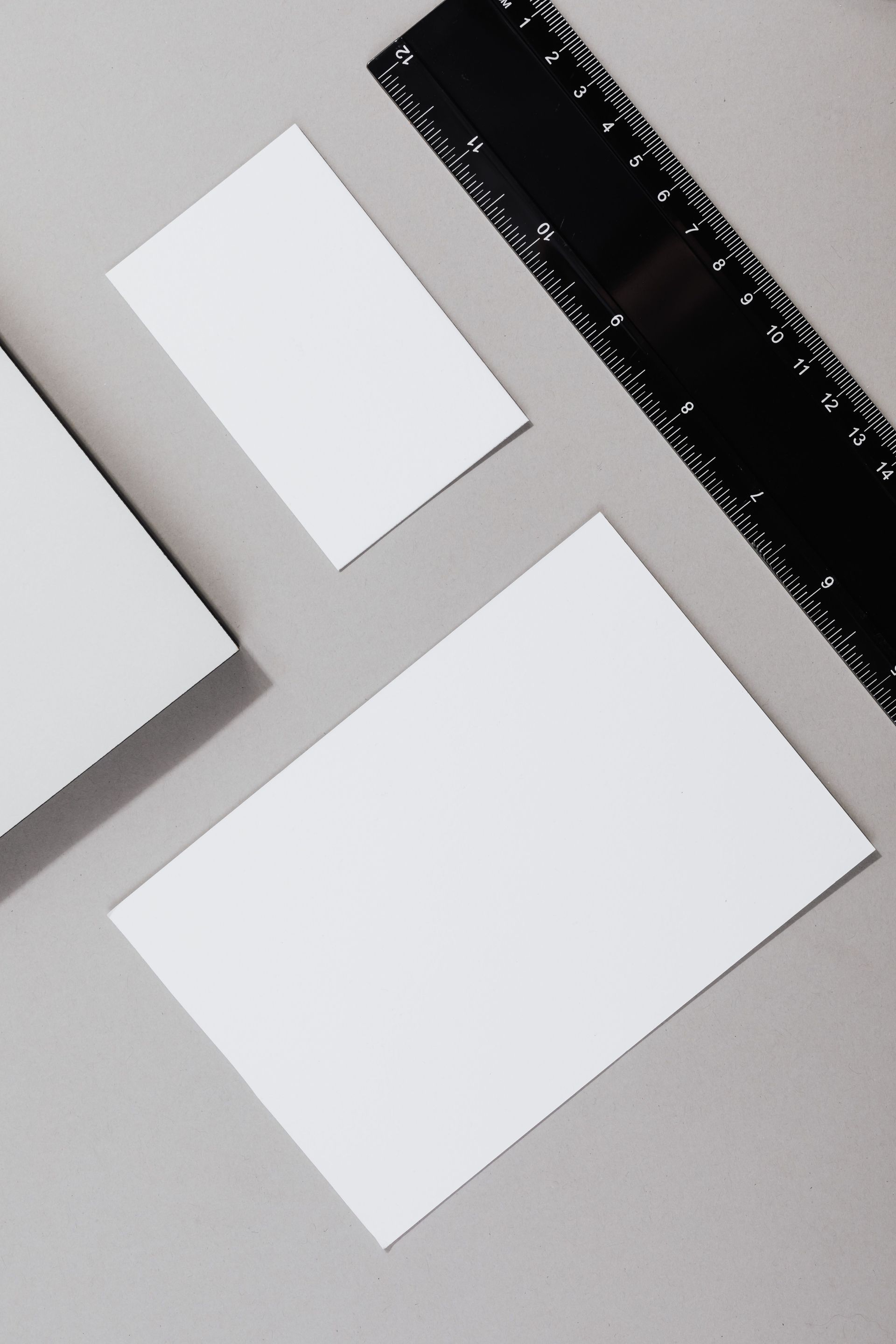 White paper cards on a gray surface beside a black ruler, viewed from above