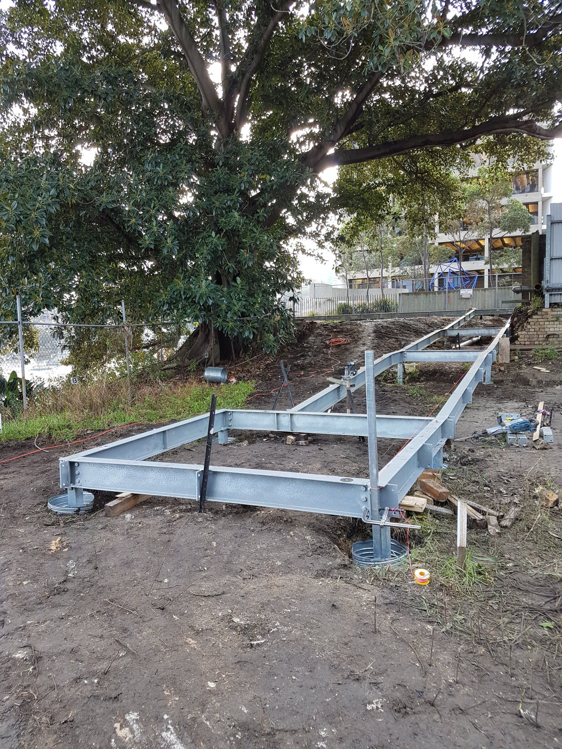 A metal frame is sitting in the dirt under a tree.