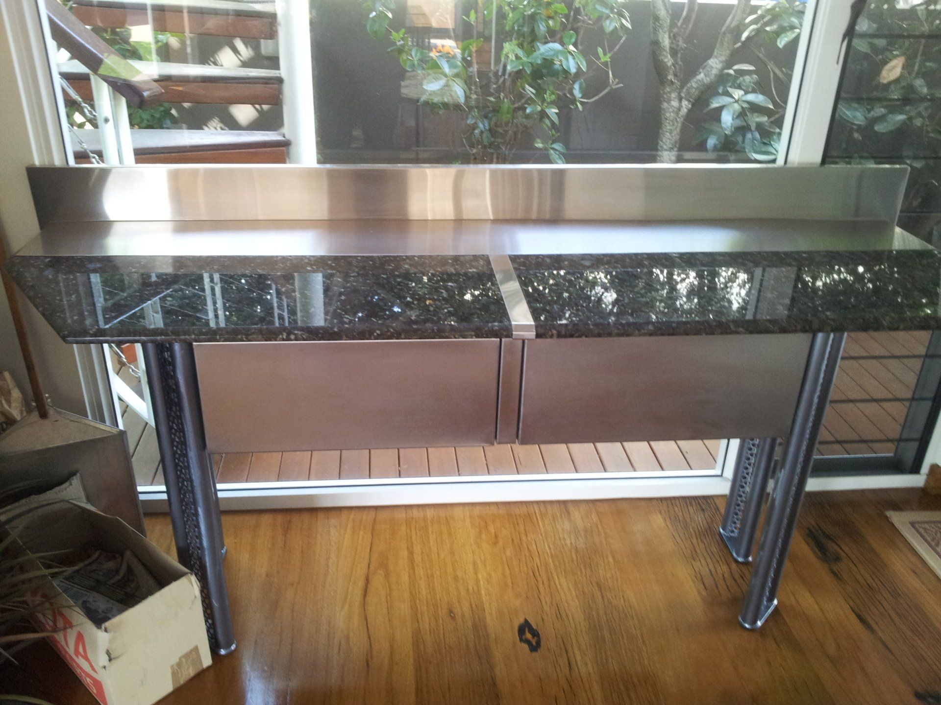 A stainless steel table with a granite top is sitting in front of a window.