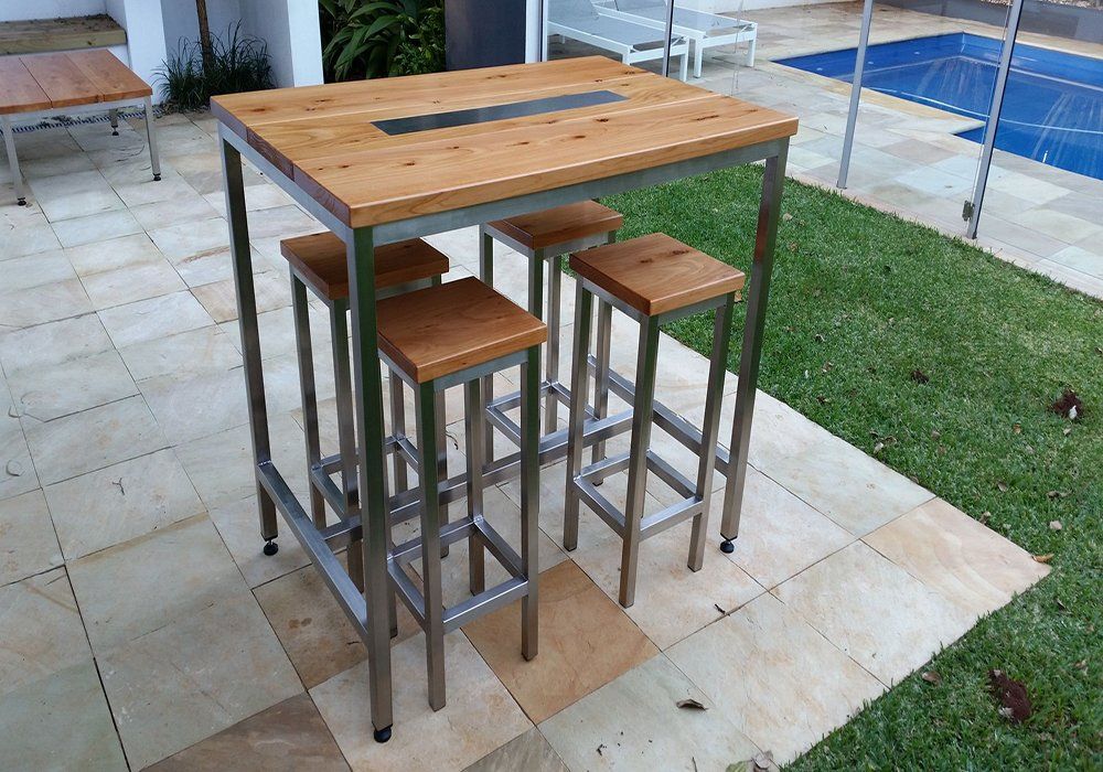 A wooden table and stools are sitting on a tiled patio next to a pool.