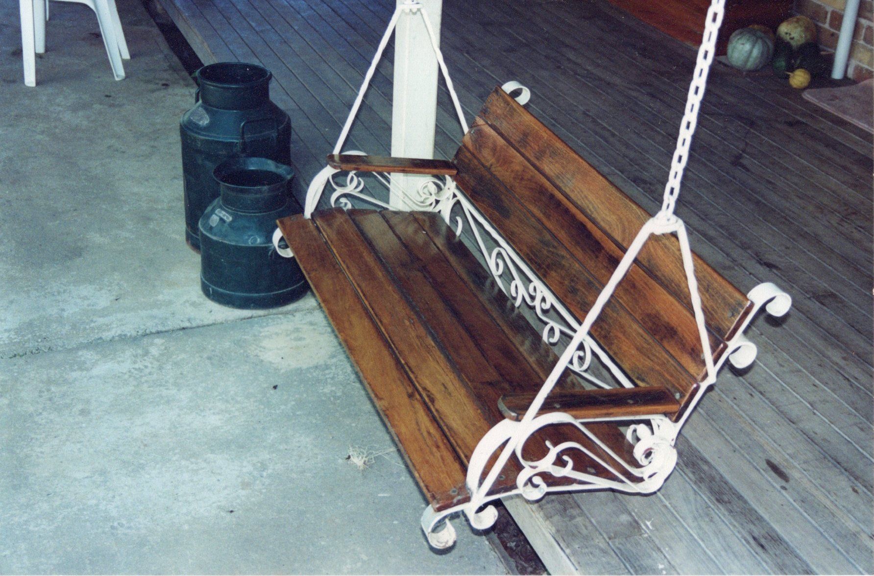 A wooden swing sits on a porch next to milk cans
