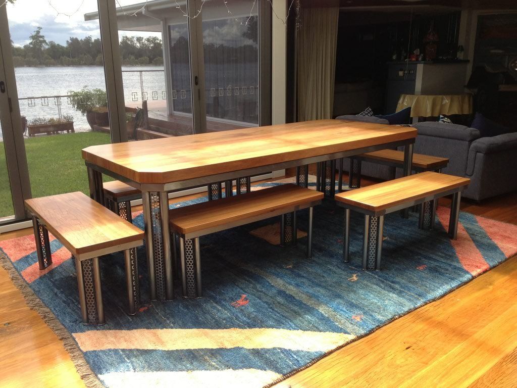 A wooden table and benches are sitting on a rug in a living room.