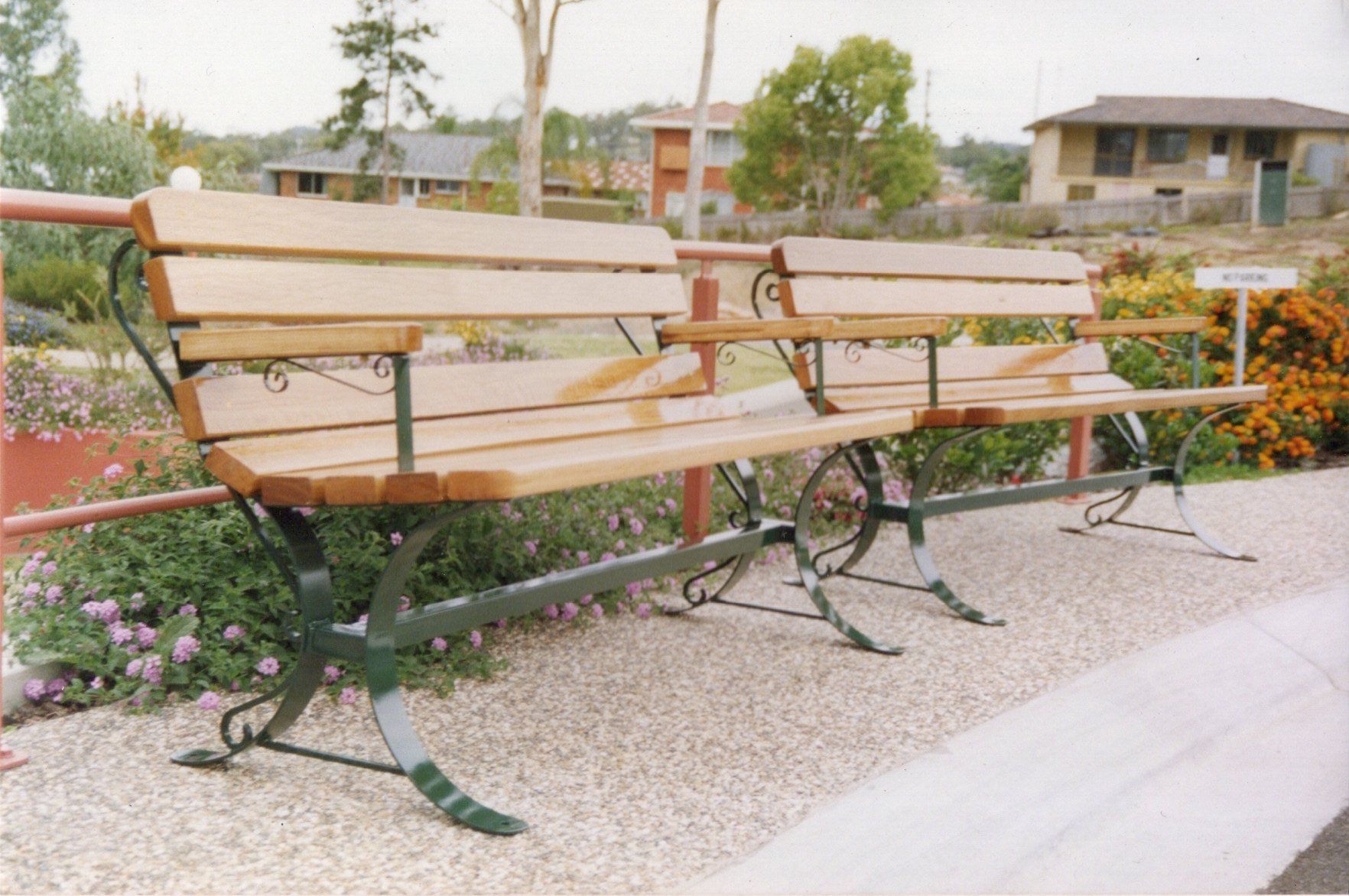 A row of wooden benches in a park with a house in the background
