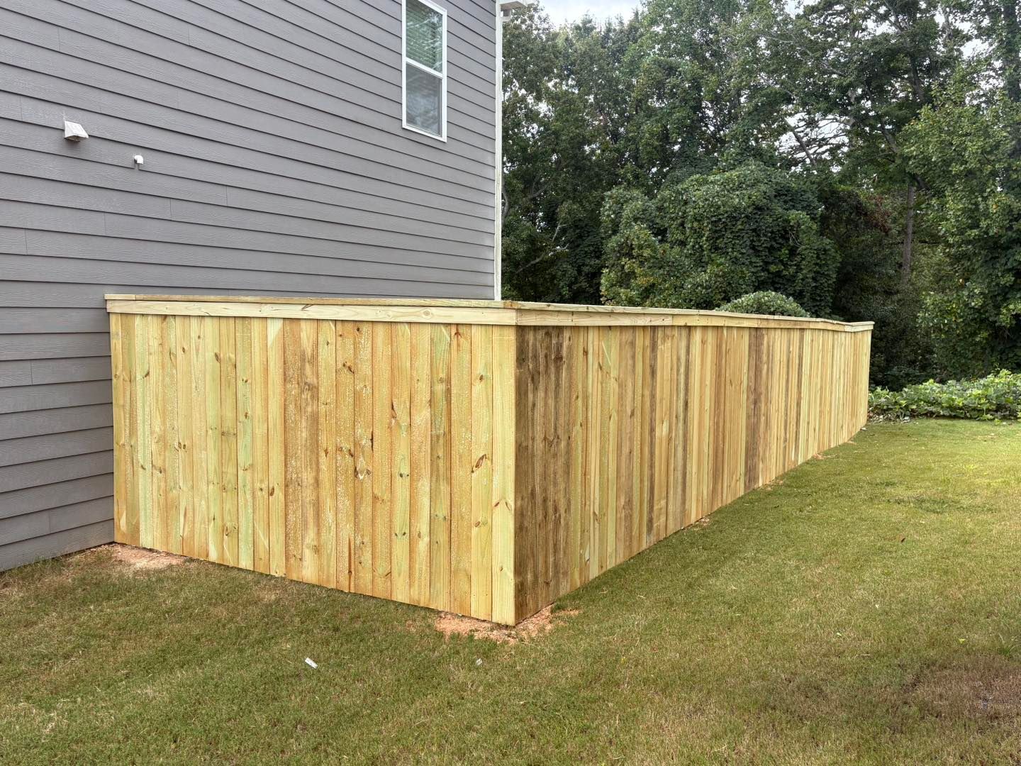 Wooden privacy fence along the side of a gray house in a grassy yard.