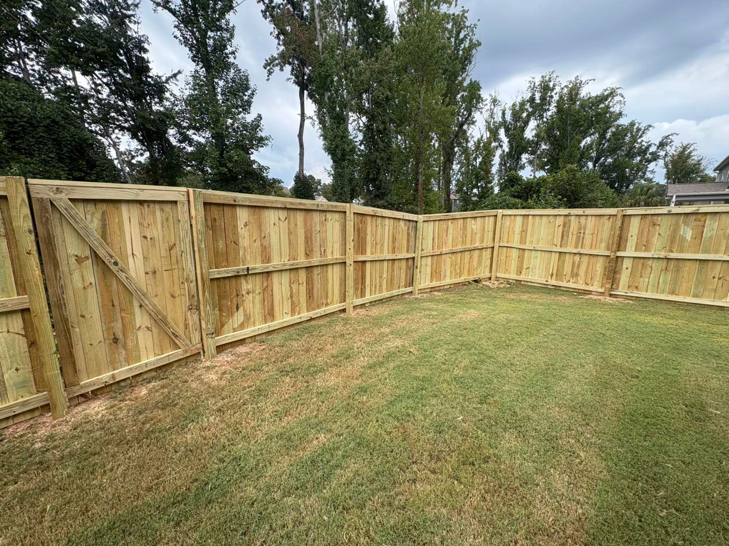Wooden privacy fence surrounding a grassy backyard under a cloudy sky.