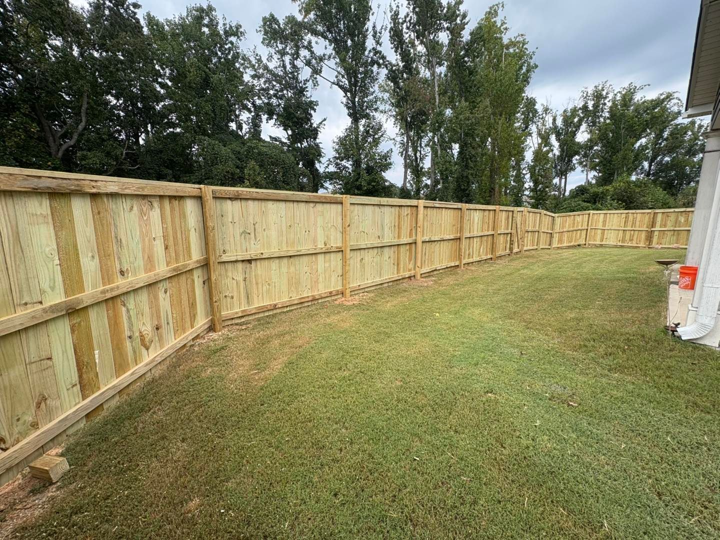 New wooden privacy fence along a grassy backyard beside a house