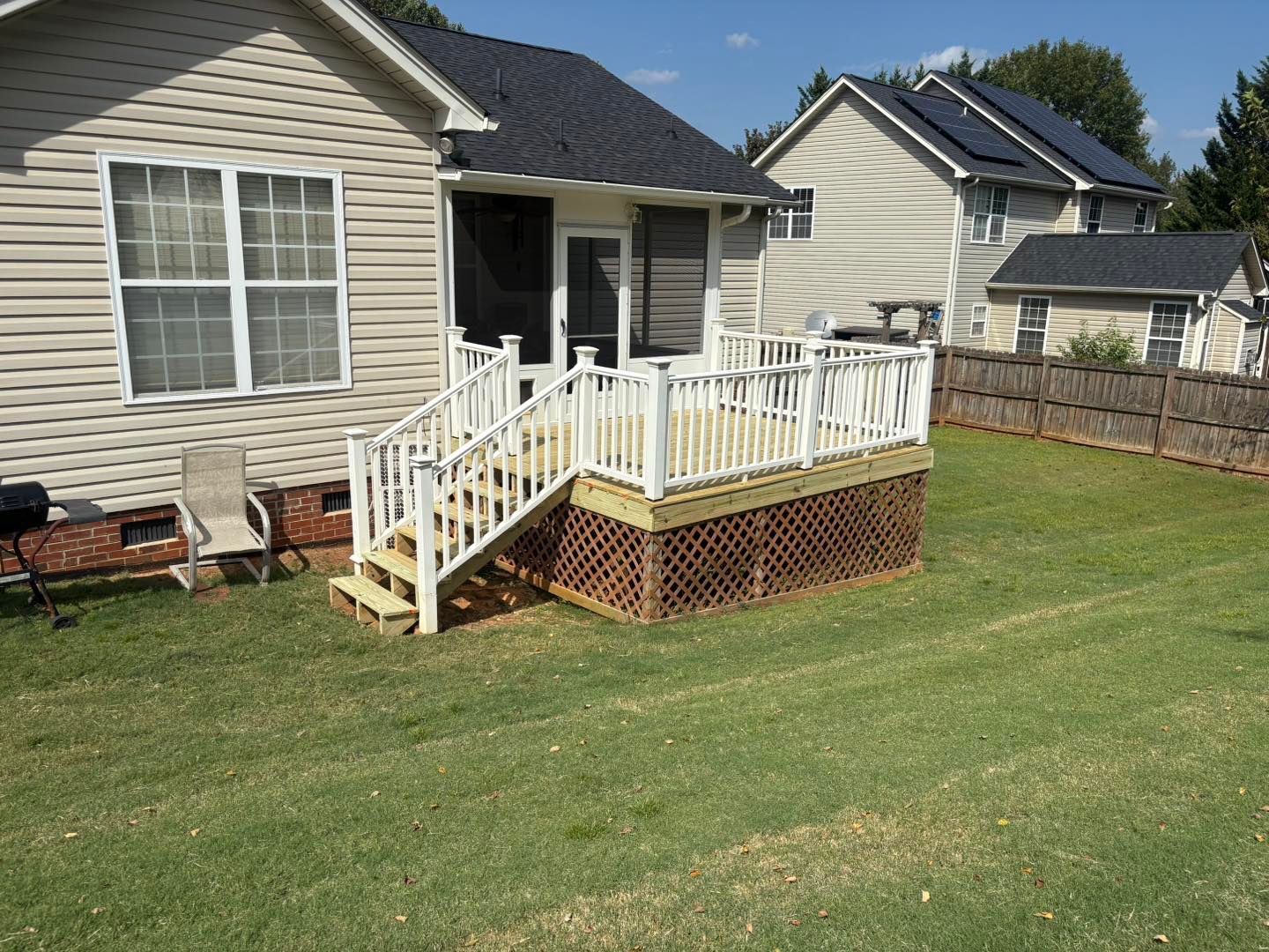 Backyard deck with white railing and stairs beside a beige house on a green lawn