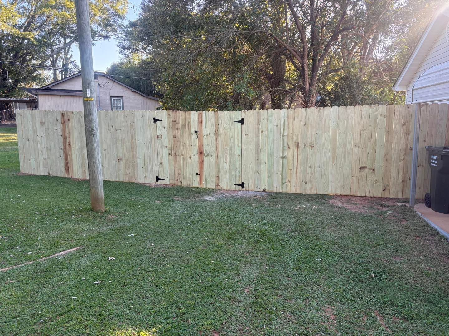 Wooden backyard fence with gate, grassy lawn, and trees in the background