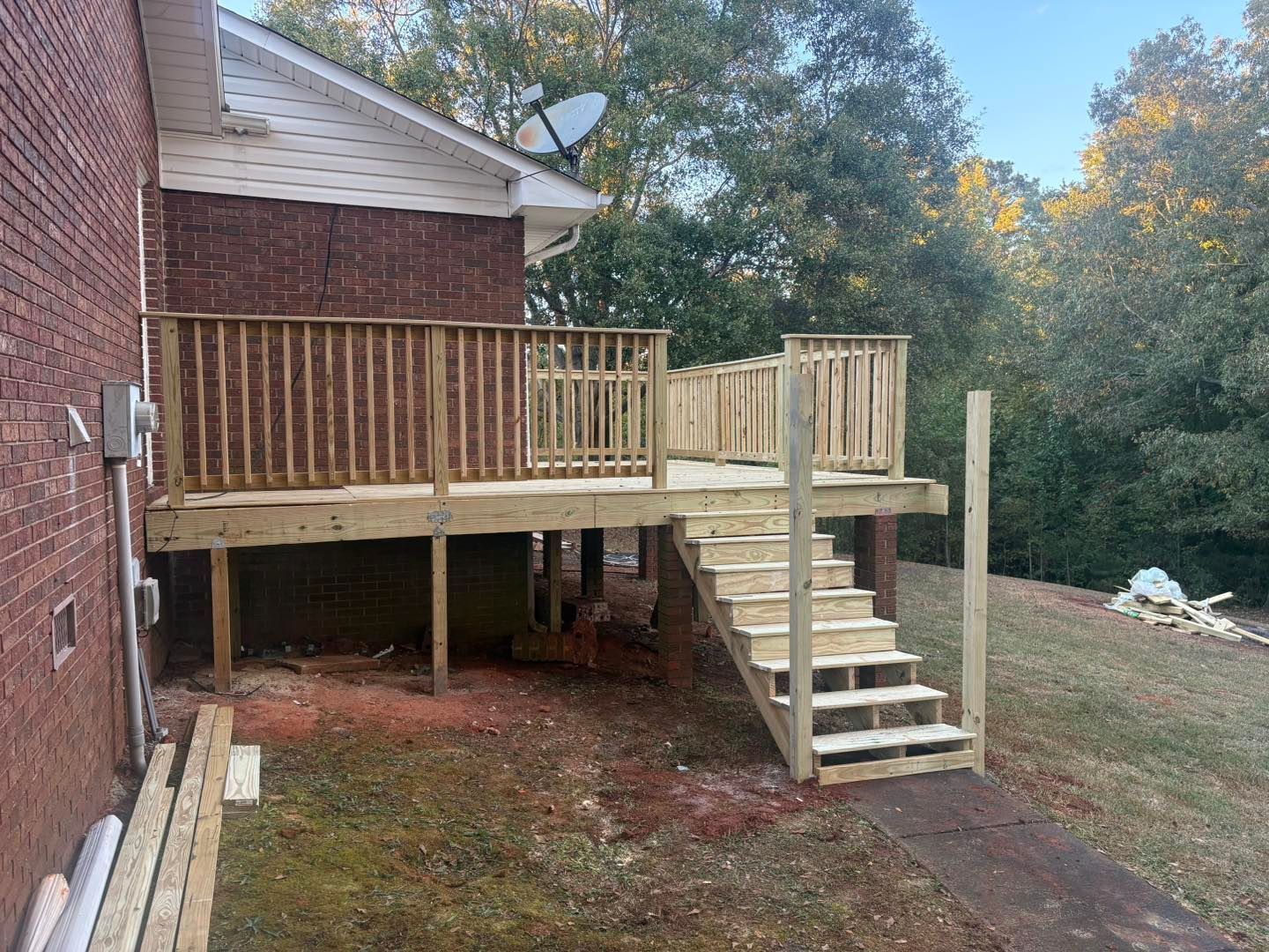 Wooden backyard deck with stairs beside a brick house, overlooking a grassy yard and trees