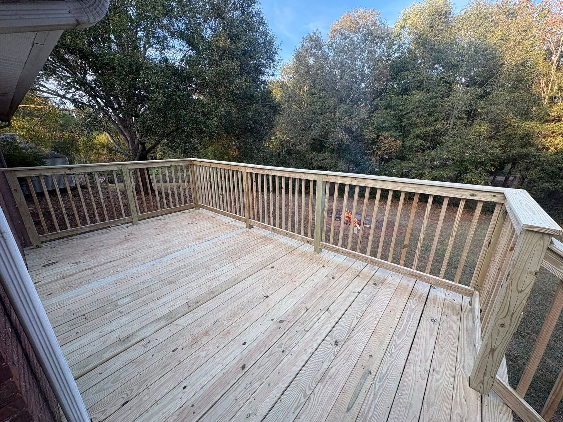 Wooden deck with railings overlooking trees and a backyard in autumn.