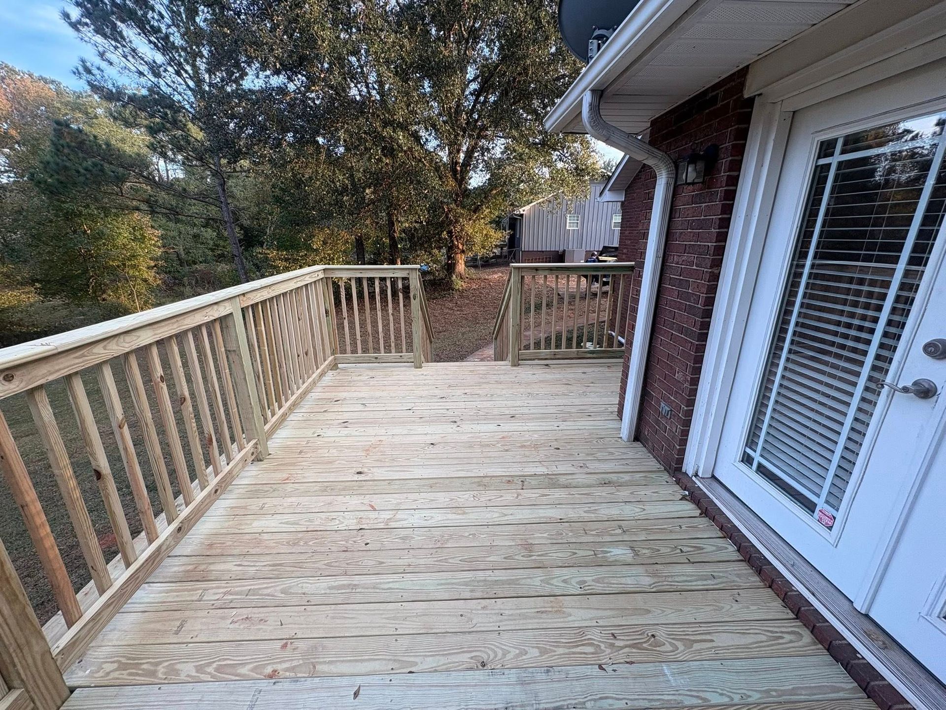 Wooden deck with railing beside a brick house and white French doors overlooking trees