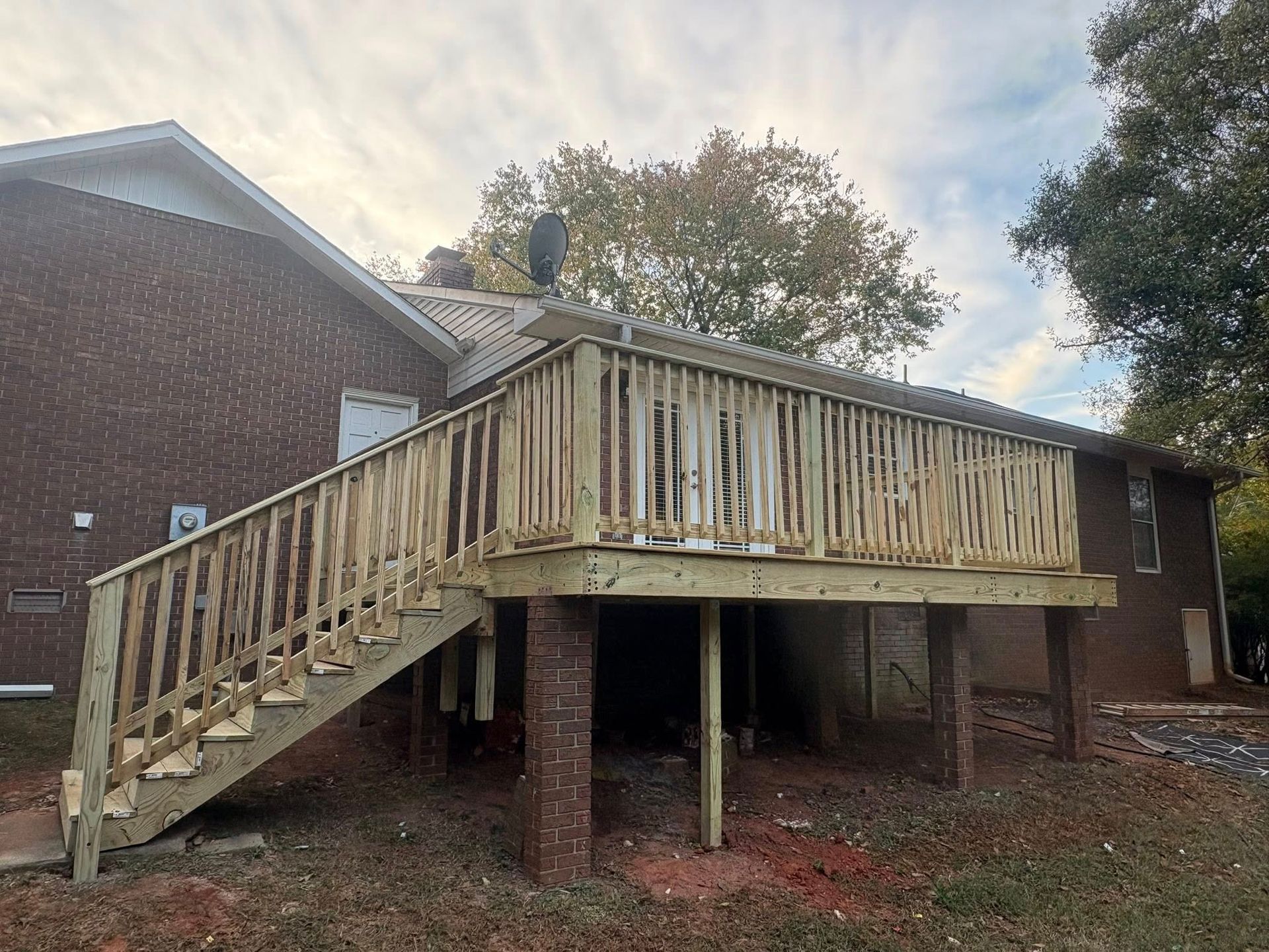 Wooden accessibility ramp with railings beside a brick house, under a raised porch