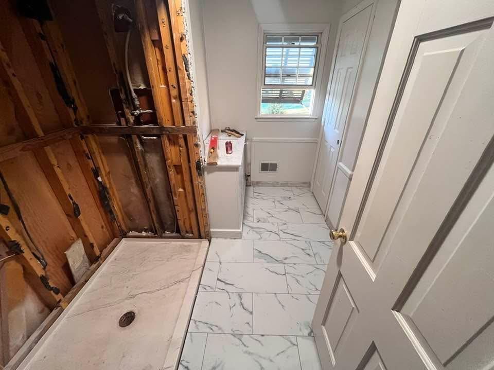 Renovation bathroom with exposed studs, marble-look tile floor, sink, and window.