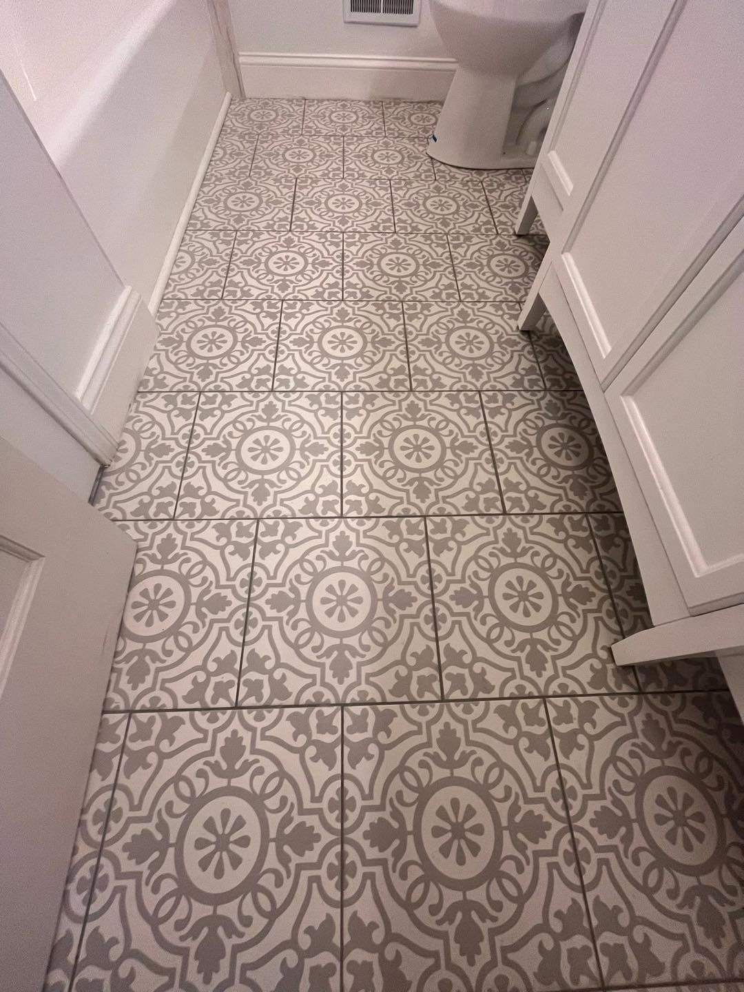 Narrow bathroom with patterned tile floor, toilet at the end, and white walls and cabinets on both sides