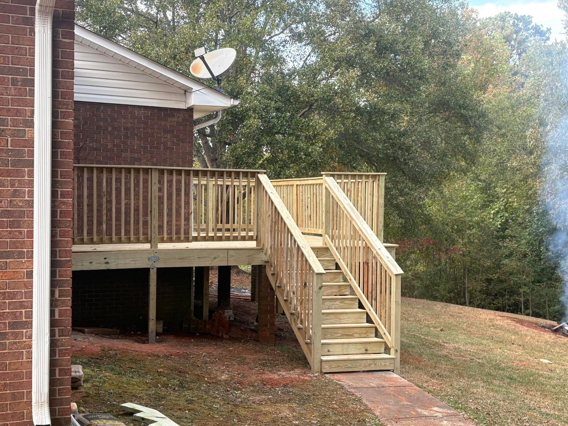 Back deck with wooden stairs on the side of a brick house, overlooking a wooded yard